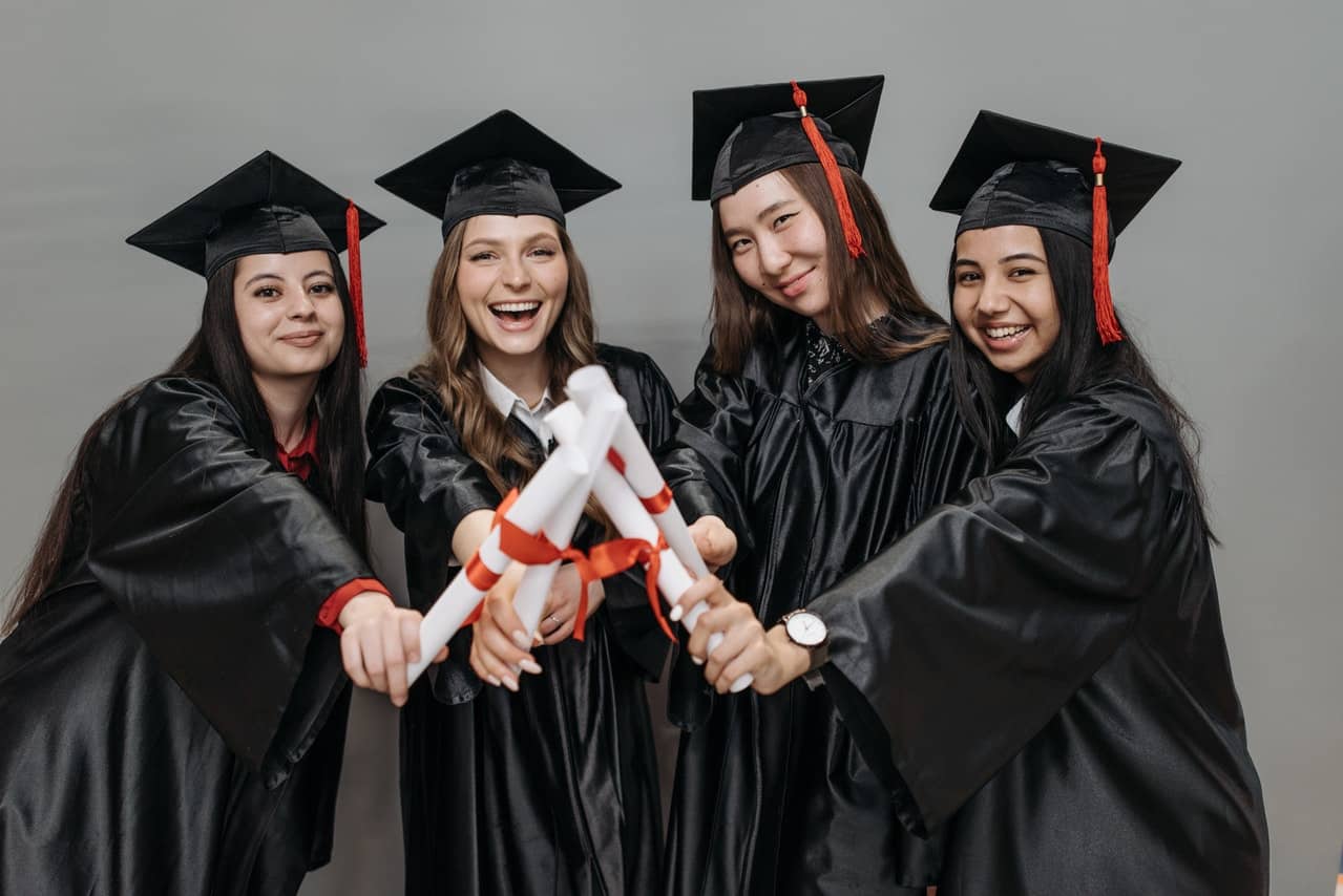 Graduandas vestidas com beca e segurando diplomas
